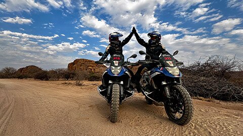 Dve vodičky z francúzskeho ženského tímu sedia vedľa seba na svojich motocykloch R 1300 GS Competition Bike a pritom si „dajú na to“.