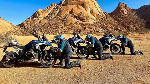 Traja vodiči mužského indického tímu kľačia pred motocyklami.