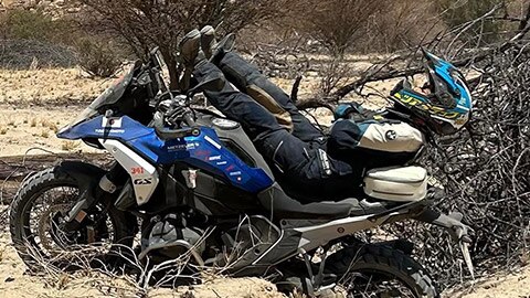 Vodička japonského ženského tímu leží na motocykli R 1300 GS. Nohy jej smerujú k riadidlám, zatiaľ čo ramená a hlava pozerajú cez zadnú časť motocykla.